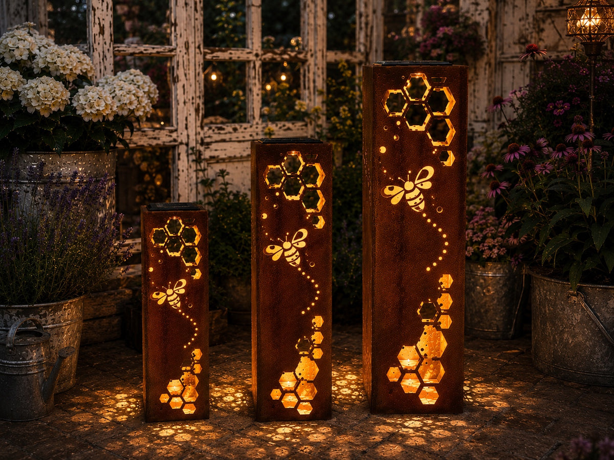 18, 24 and 32 inch rusted steel honeycomb bee solar luminaries glowing in a cottage pollinator garden