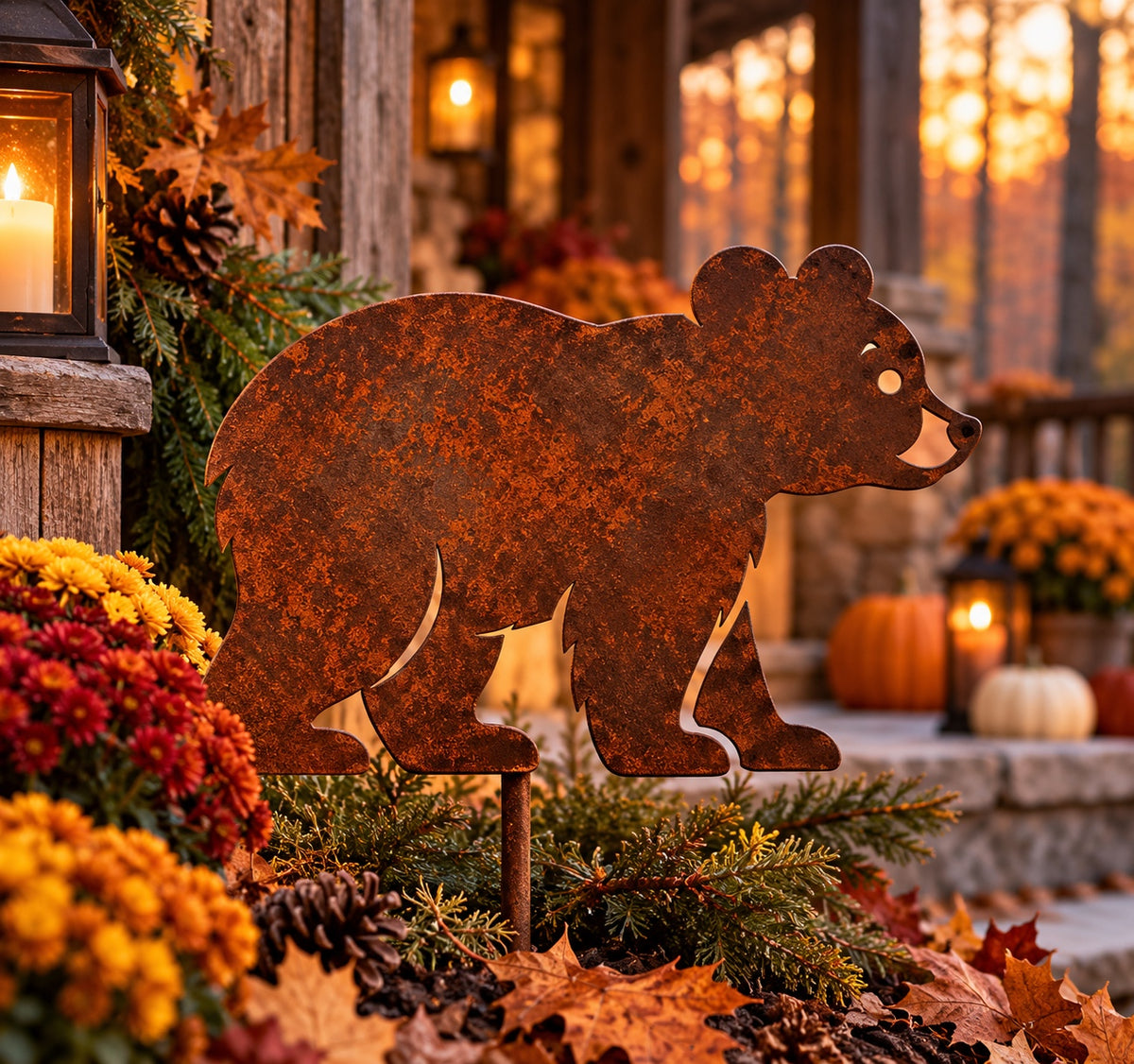 Rusted Woodland Bear Metal Garden Stake with rounded ears and open face and leg details, styled among autumn mums and evergreen branches beside a cabin porch.